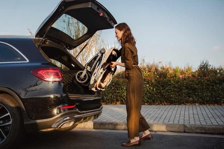 Woman holding a folded pet stroller beside an open car boot.
