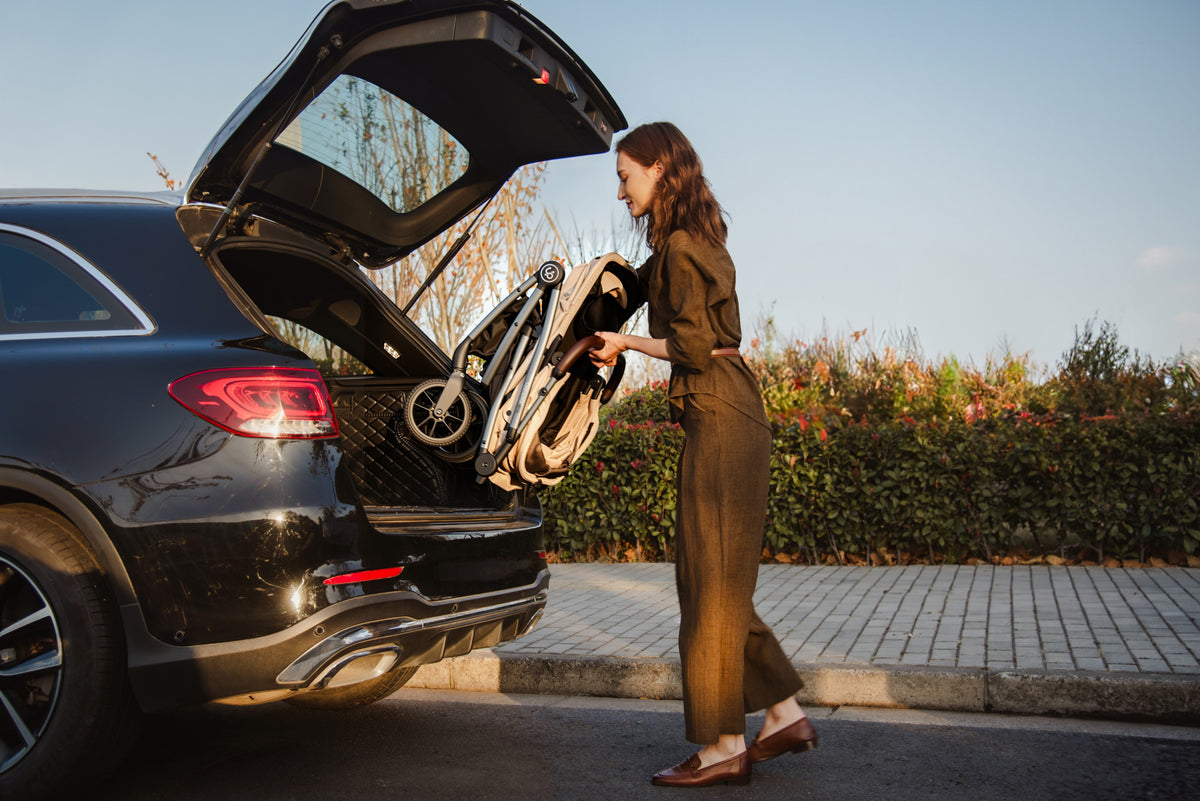 A woman lifting a folded Uppapets Hybrid pet stroller into a car boot.